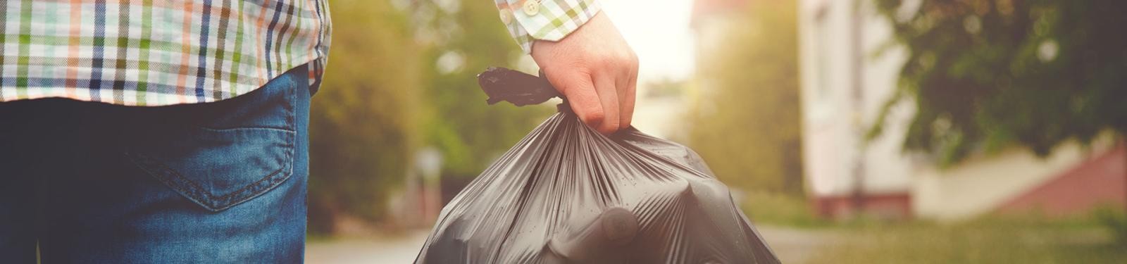Restmüll Ein Mann hält einen vollen Müllbeutel in der Hand. dahinter ist eine Straße im Wohngebiet zu sehen