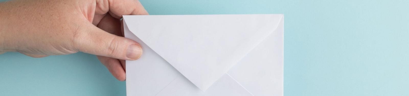 Aktuelles Eine Hand hält einen Briefumschlag vor hellblauem Hintergrund.