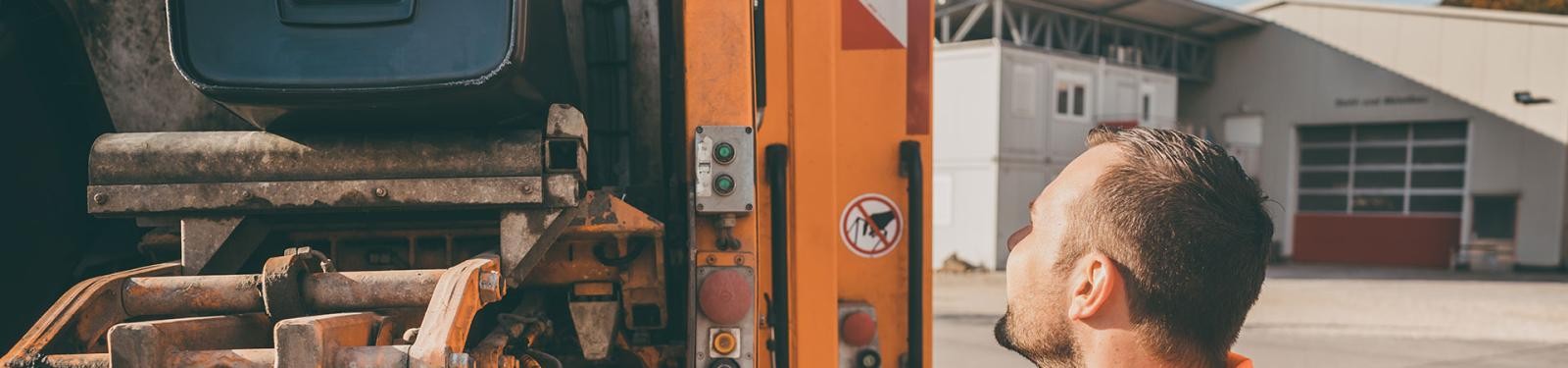 Gewerbeabfall entsorgen Ein Müllwerker bedient das Müllfahrzeug; die Tonne wird entleert.