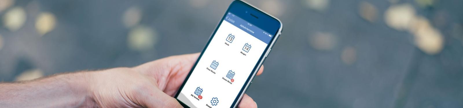 Unsere AbfallAPP Eine Hand hält ein Smartphone. Auf dem Display ist die geöffnete Abfall-App zu sehen.