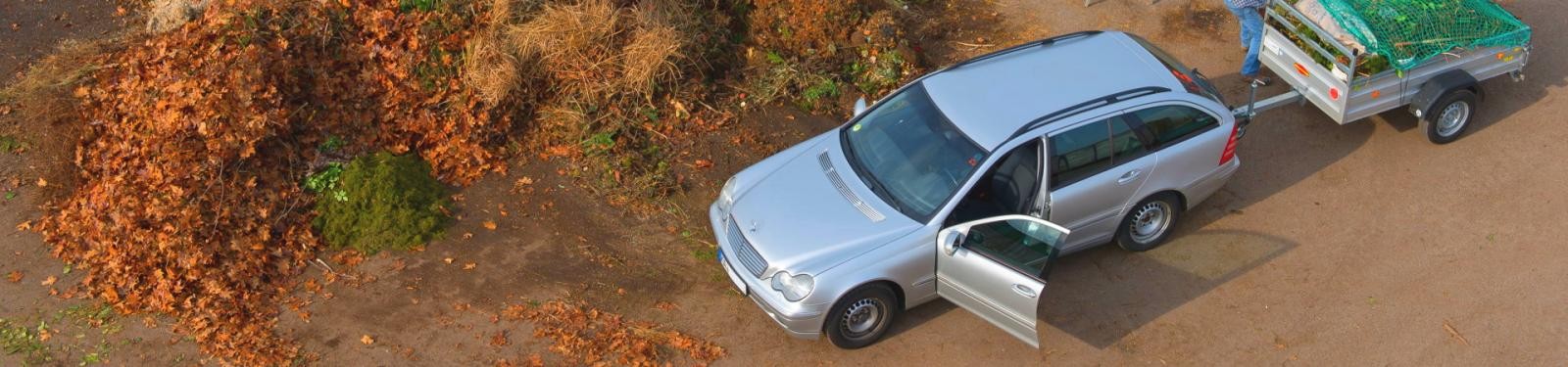 Grünabfallsammelplätze Ein Auto mit Anhänger, das Grünschnitt anliefert