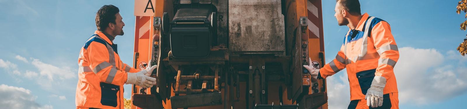 Abfuhrkalender Zwei Müllwerker stehen am Müllfahrzeug; die Tonne wird gekippt.