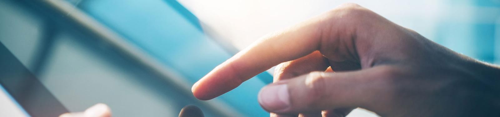 Formulare/Downloads Hände mit Tablet in der Hand, dahinter Sonneneinstrahlung.