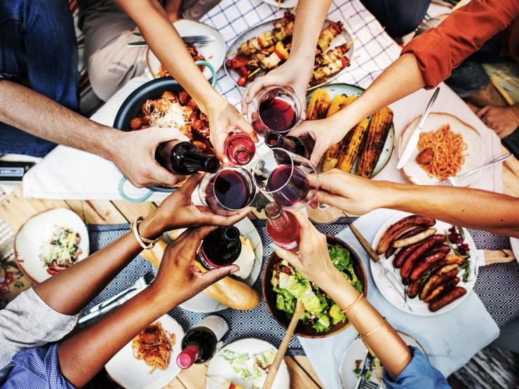 Grillgut auf einem Tisch, Menschen halten Gläser darüber und stoßen an Grillgut auf einem Tisch, Menschen halten Gläser darüber und stoßen an