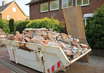 Ein mit Ziegeln befüllter Container steht vor einer Hecke.