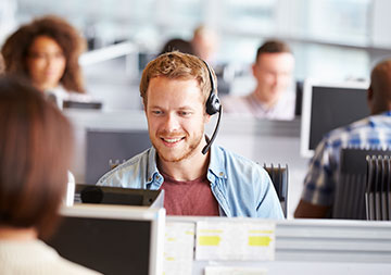 Ein Mann mit Headset sitzt in einem Großraumbüro am Schreibtisch.