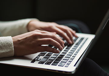 Hände tippen etwas in einen geöffneten Laptop.