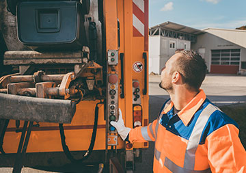 Tonne bestellen Ein Müllwerker bedient das Müllfahrzeug; die Tonne wird entleert.