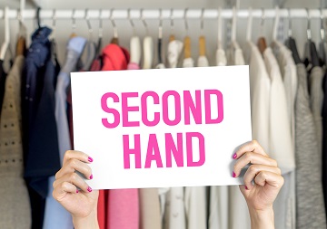 Second-Hand Kleidung Eine Person hält ein Schild mit der Aufschrift "Second Hand" hoch, im Hintergrund befindet sich ein Kleiderständer