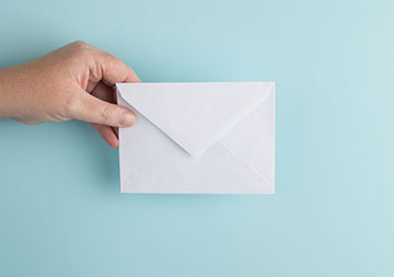 Eine Hand hält einen Briefumschlag vor hellblauem Hintergrund.