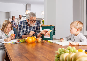 Bioabfall Ein älterer Mann sitzt mit zwei Kindern am Esstisch; auf dem Tisch befindet sich Obst und ein Bioabfallsammelbehälter